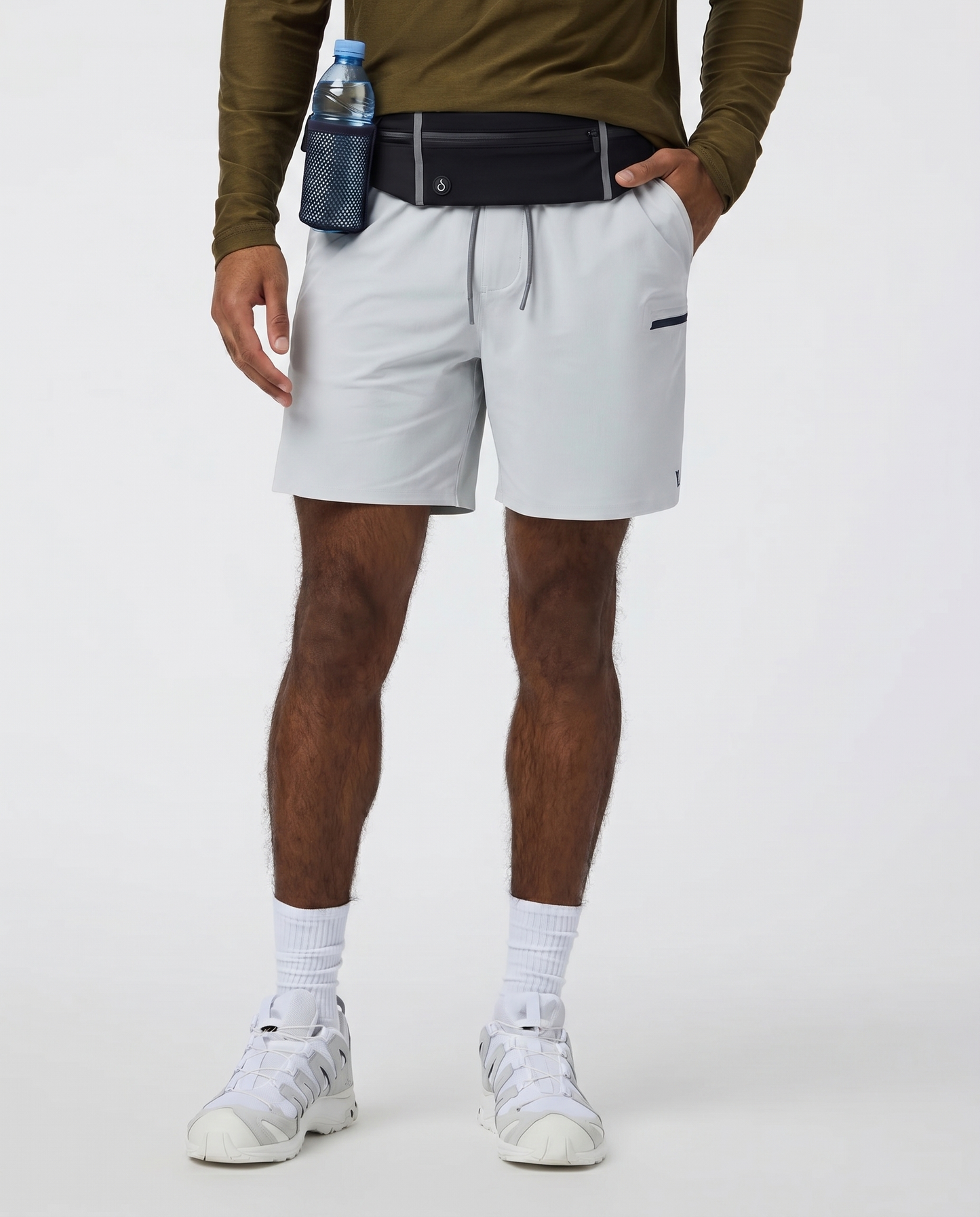 Person wearing white shorts, a green long-sleeve shirt with Farivive waistbag slightly tucked underneath, and white sneakers on a light gray background.