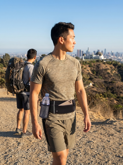 Two people hiking and one is using Farivive waistbag that has a bottle carrier bottles on a trail with a city skyline in the background.