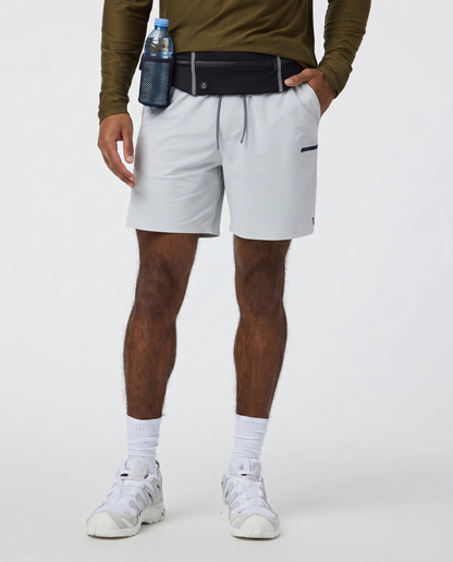 Person wearing white shorts, a green long-sleeve shirt with Farivive waistbag slightly tucked underneath, and white sneakers on a light gray background.